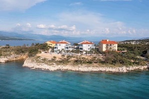 A coastal property with multiple buildings, a beach, and a view of the sea and mountains.