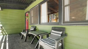 A covered porch with two wooden chairs and a table, green walls, and large windows. - Village and Lake Escape - Hot Tub, Walk to Lake & Village, Barbecue (Big Bear Lake)