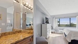 Ein modernes Schlafzimmer mit Granitplatte, einem großen Spiegel, einer Kommode, einem Bett und Blick ins Freie.
