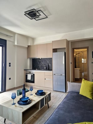 A modern kitchen with a marble countertop, stainless steel appliances, and a dining area with a table set for two. - Volos Terra Deluxe Residences (Volos)