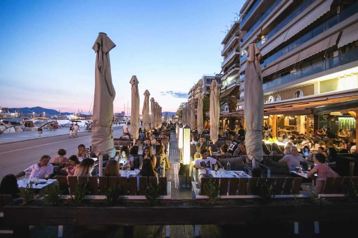 A waterfront dining area with outdoor seating, umbrellas, and a view of the marina.