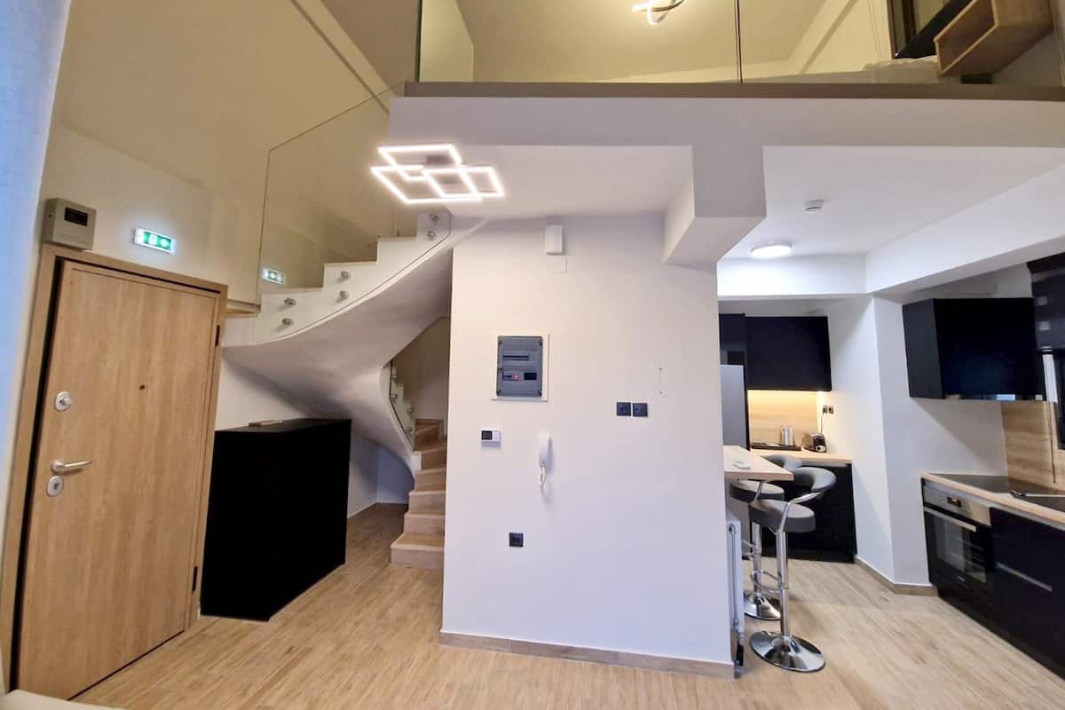 A modern kitchen with a built-in stove, a dining area with bar stools, and a staircase leading to an upper level.