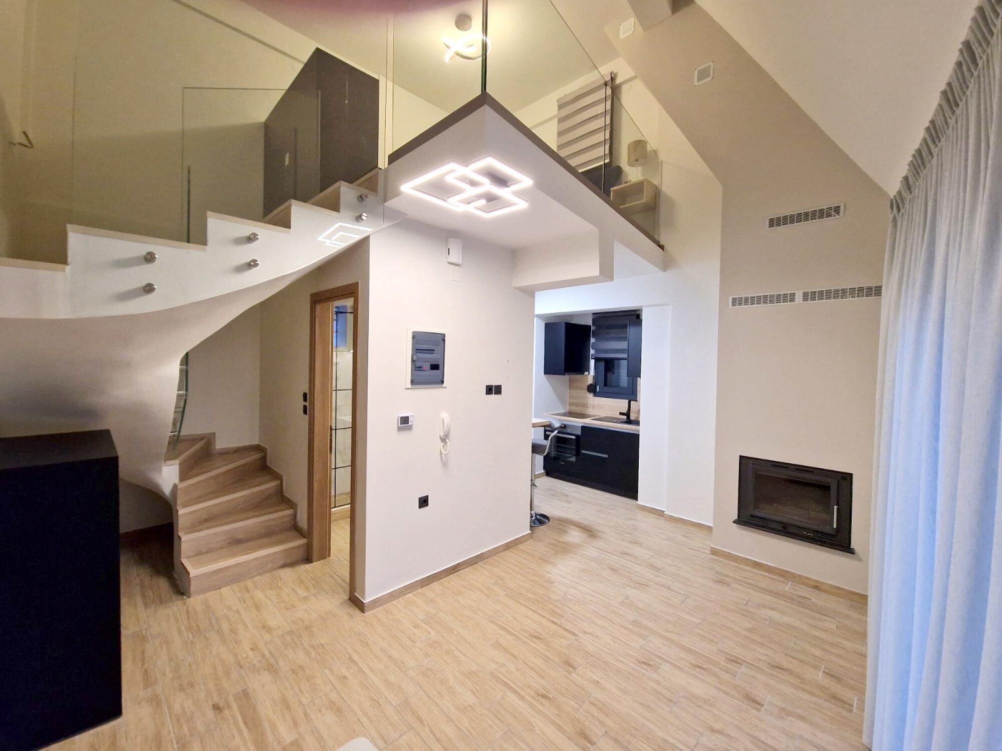 Un interior moderno con una escalera que sube a un altillo, una zona de cocina y una chimenea.