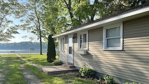 A single-story house with a front porch, a pathway leading to the door, and a view of a lake in the background.