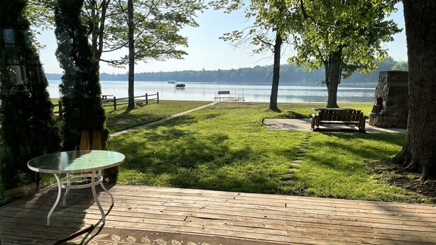 A deck with a glass table, a bench, and a view of a lake with boats.