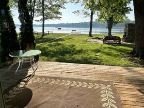 Een terras met een glazen tafel, een bank en uitzicht op een meer met bootjes.