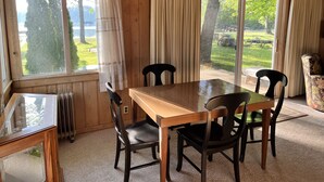 A wooden-paneled room with a large table and chairs, large windows with curtains, and a view of a green landscape.