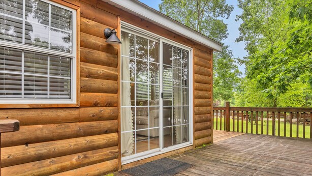 Une cabane en rondins dotée d’une grande porte-fenêtre coulissante, d’une terrasse et d’une clôture en bois.