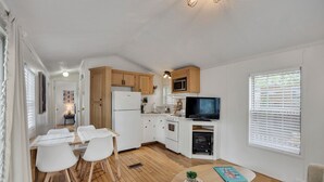 Une cuisine compacte avec des meubles blancs, un four à micro-ondes, une cuisinière et un téléviseur. On y trouve une table à manger avec des chaises et un petit tapis.