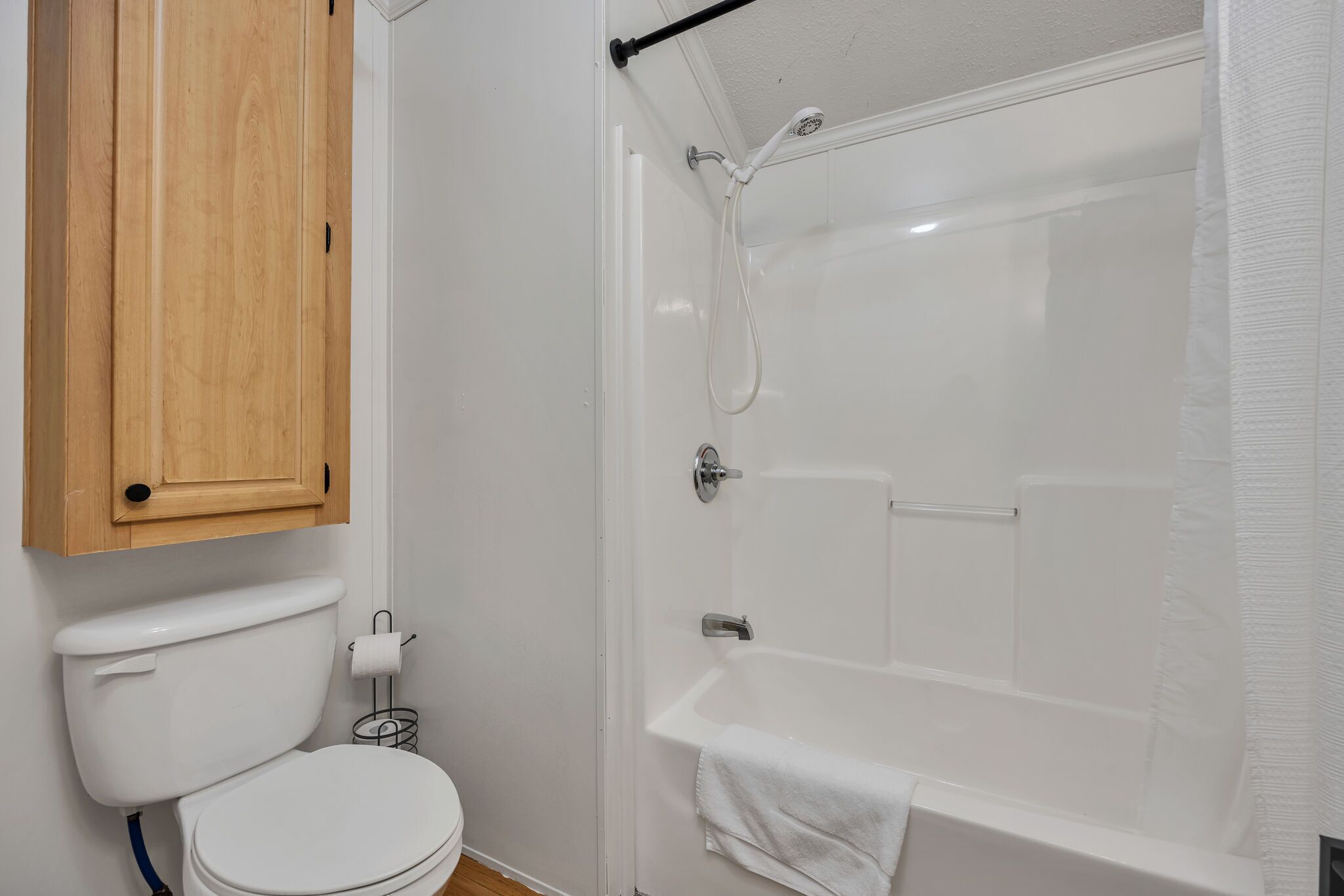 A bathroom with a toilet, wooden cabinet, and a glass-enclosed shower with a bathtub.