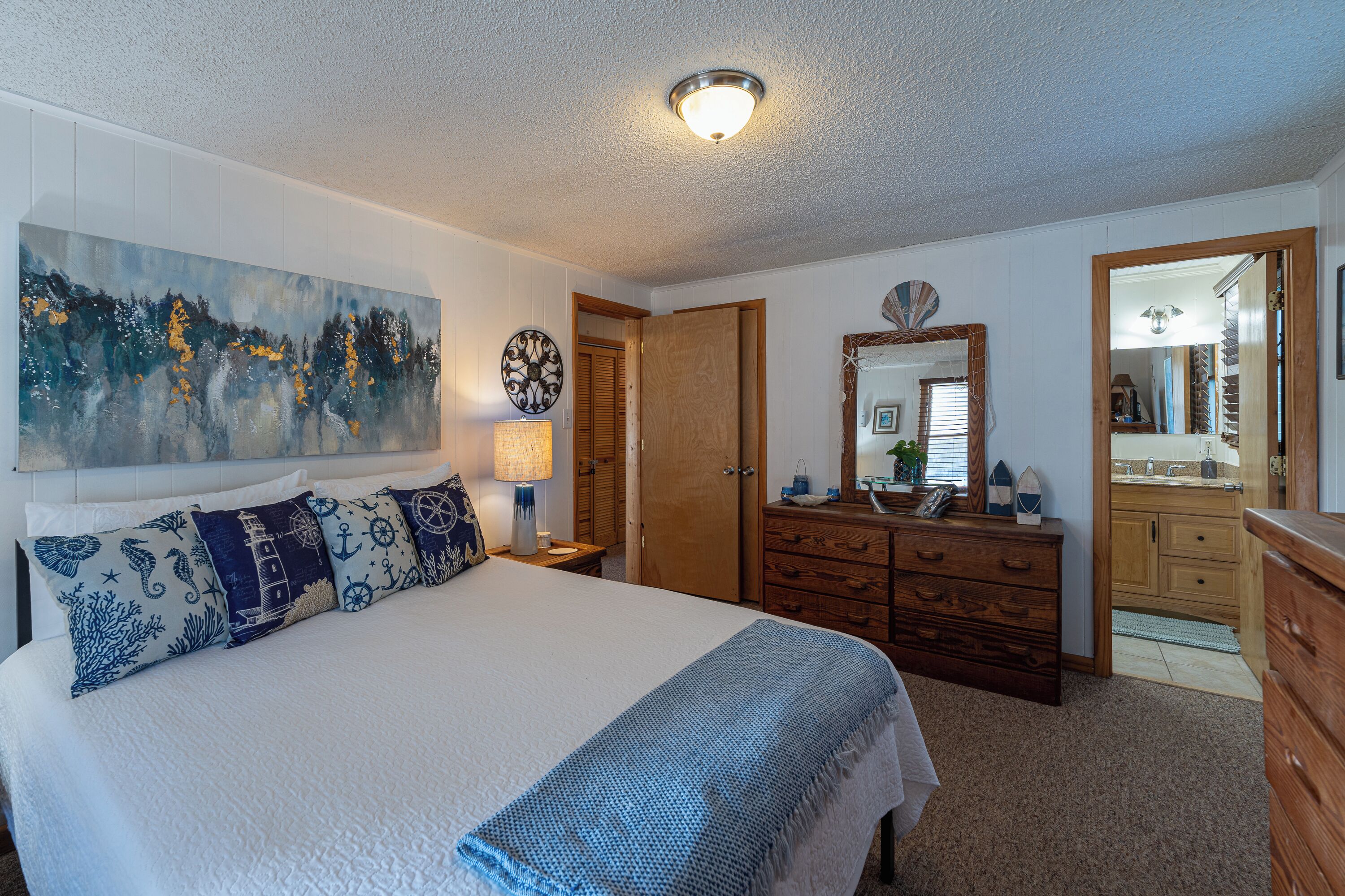A bedroom with a large bed, a dresser, a mirror, and a painting on the wall.