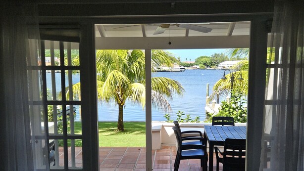 An open door leading to a patio with a view of a body of water, palm trees, and a tiled floor. - The Anchorage #5 a 3 bedroom Waterfront Condo in Rodney Bay (Rodney Bay)