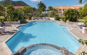 Ein Pool mit Liegestühlen und Whirlpool, umgeben von Palmen und Gebäuden.