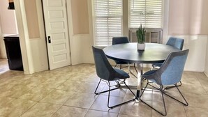 Un comedor con una mesa redonda y cuatro sillas, una planta en maceta y una puerta.