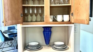 Un mueble de madera con estantes que contienen platos, vasos y un jarrón azul.