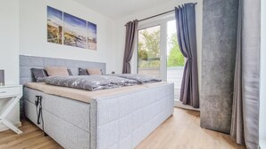 A modern bedroom with a large bed, a bedside table, and a window with curtains. - Cozy home in Tossens with sauna (Tossens)