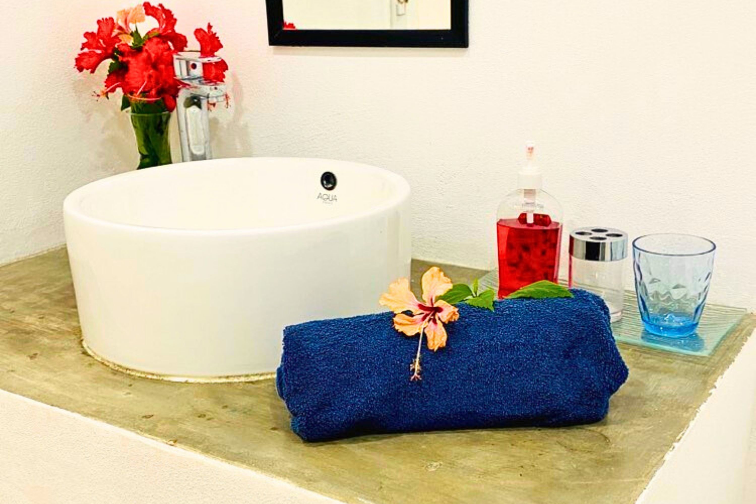 A bathroom with a white sink, a blue towel, a glass of water, and a vase with red flowers.