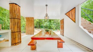 A modern interior with a long wooden table, bamboo pillars, and a view of a lush garden. - Antema Lodge (Tamarindo)
