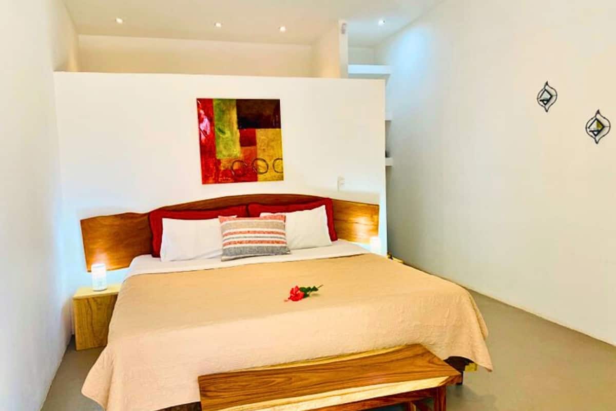 A modern hotel room with a large bed, a wooden headboard, and a colorful abstract painting on the wall.