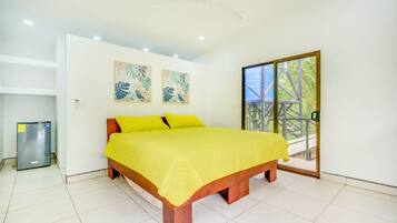 A bedroom with a bed, a ceiling fan, a refrigerator, and a sliding glass door to an outdoor area.