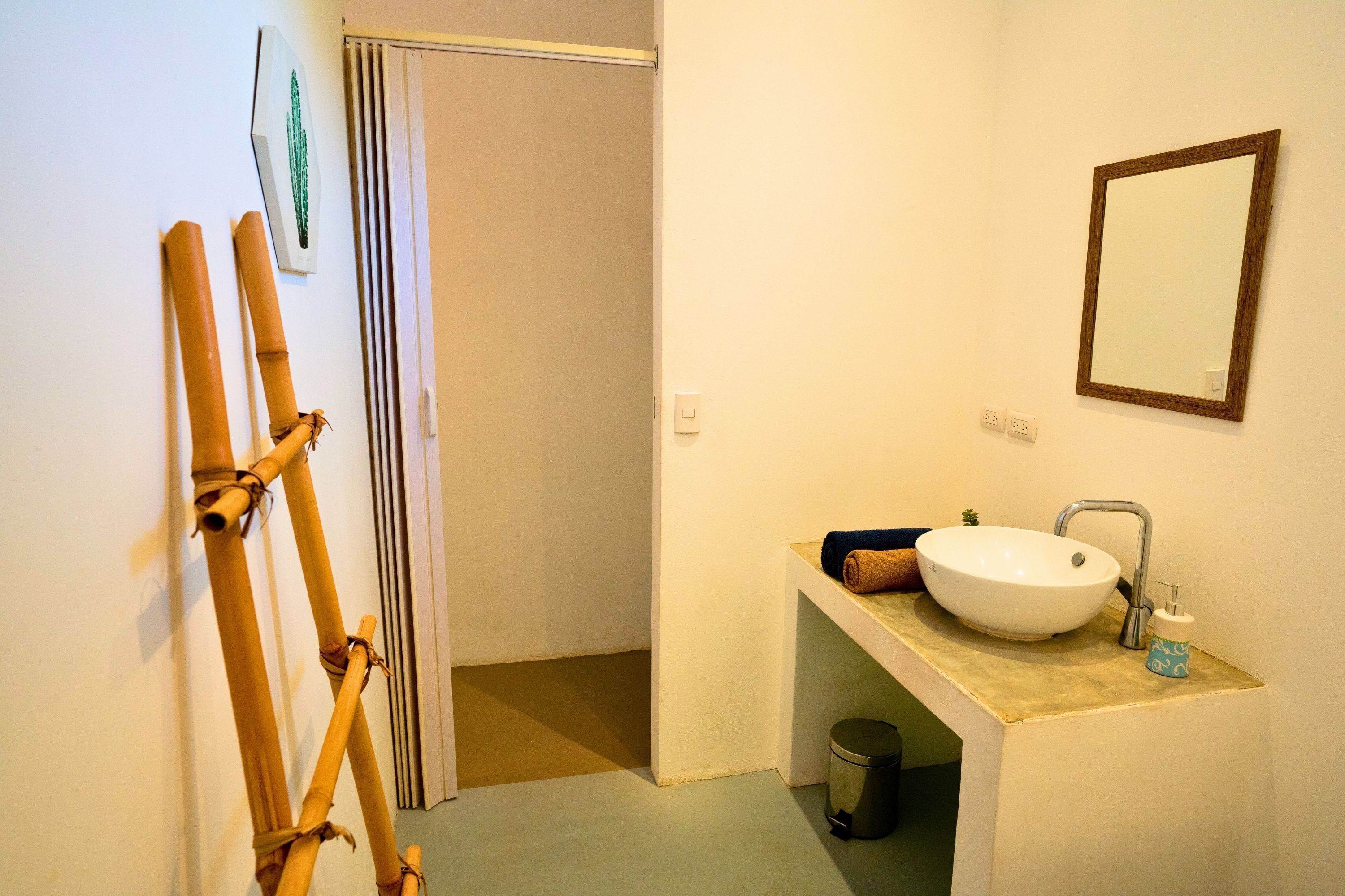 A bathroom with a white sink, a mirror, and a toilet. There is a towel rack with a towel and a small trash bin.