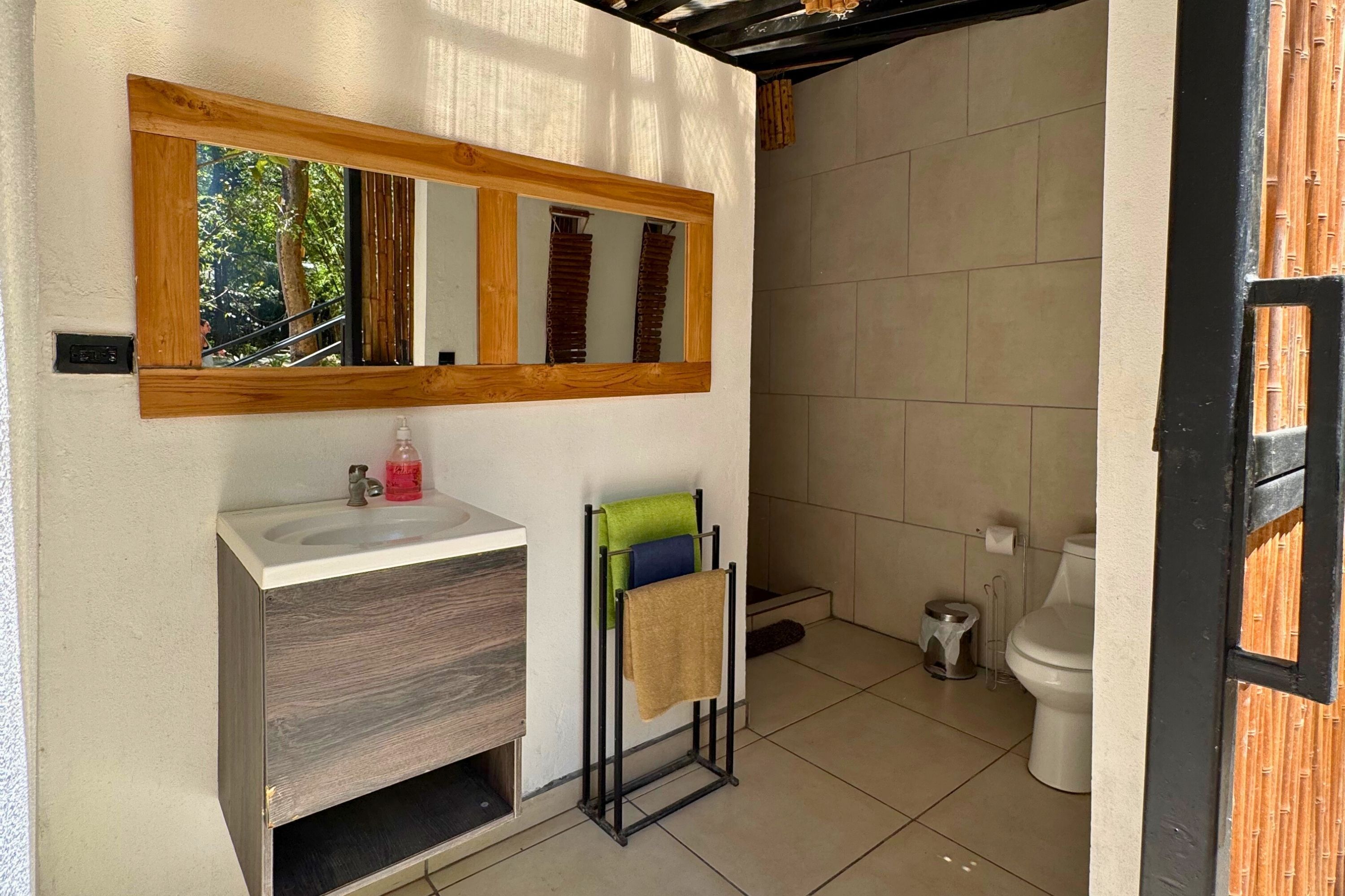 Uma casa de banho com toucador de madeira, espelho, porta-toalhas e sanita.