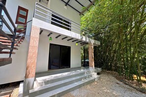 A modern two-story building with a staircase leading to a balcony, surrounded by bamboo. - Antema Lodge (Tamarindo)