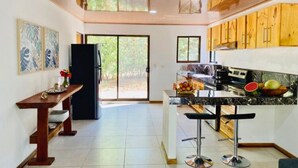 A modern kitchen with wooden cabinets, a marble countertop, and a built-in bar area with stools. - Antema Lodge (Tamarindo)