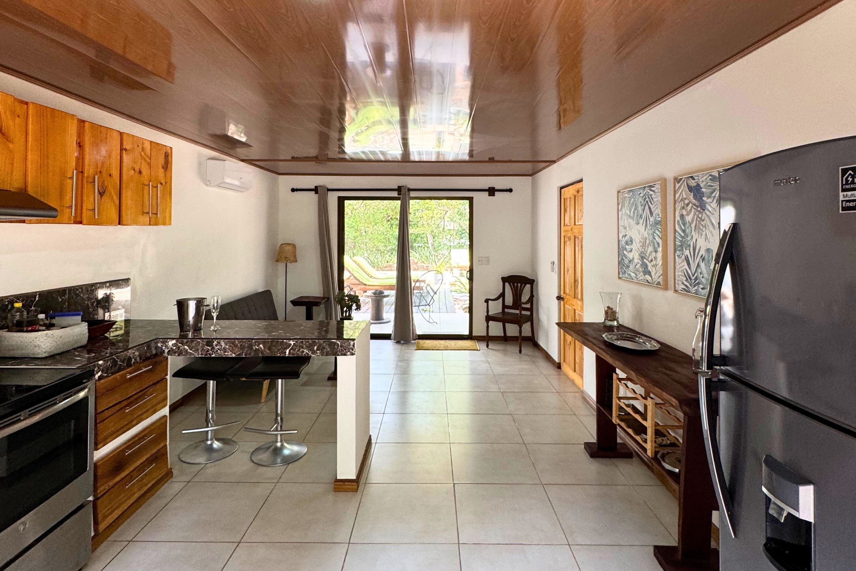 Cozinha moderna com armários de madeira, geladeira preta e área de jantar com banco e cadeiras.