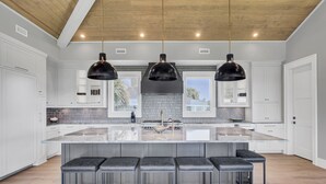 A modern kitchen with a large island, pendant lighting, and bar stools.