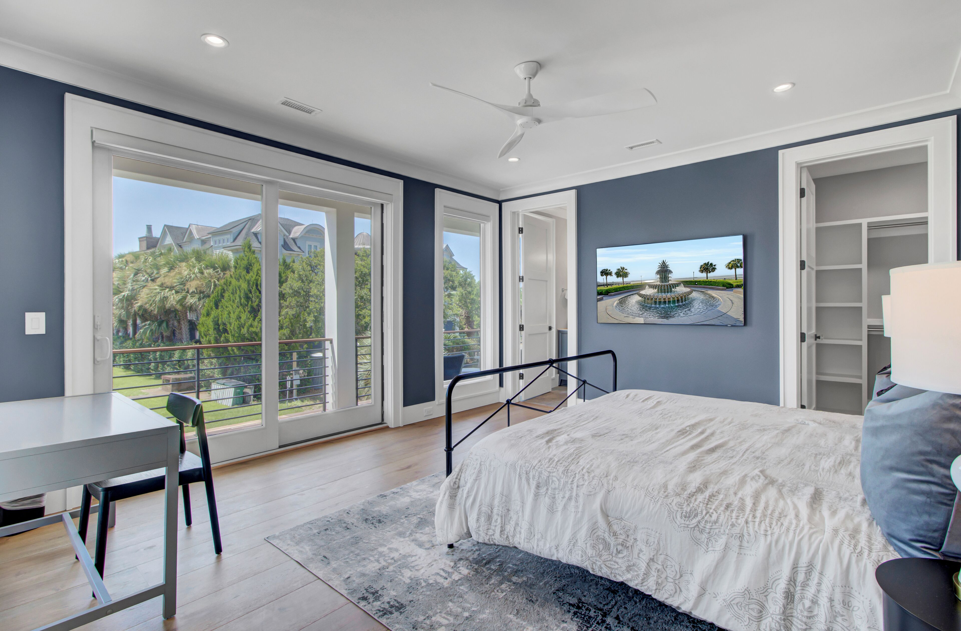 Un dormitorio con cama, escritorio y silla. Hay un ventanal con vistas a árboles y un edificio.