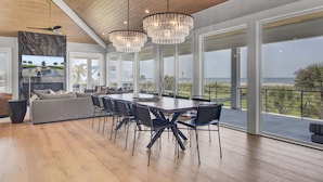 A spacious dining area with a large table and chairs, a modern kitchen with a marble backsplash, and large windows offering a view of the ocean.