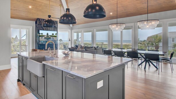 A spacious kitchen with a large island, modern pendant lights, and a view of the ocean.