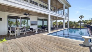 A modern outdoor deck with a pool, seating area, and a covered section with a grill.