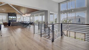 A spacious living area with a high ceiling, large windows, and a modern chandelier.