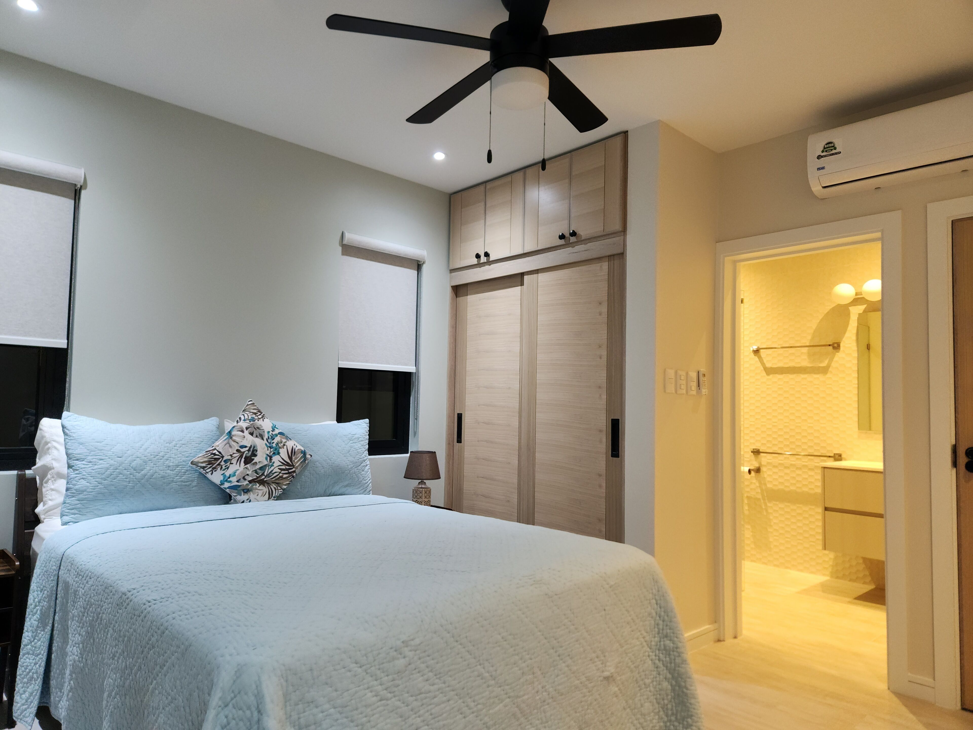 A bedroom with a bed, a ceiling fan, a wardrobe, and an air conditioning unit.