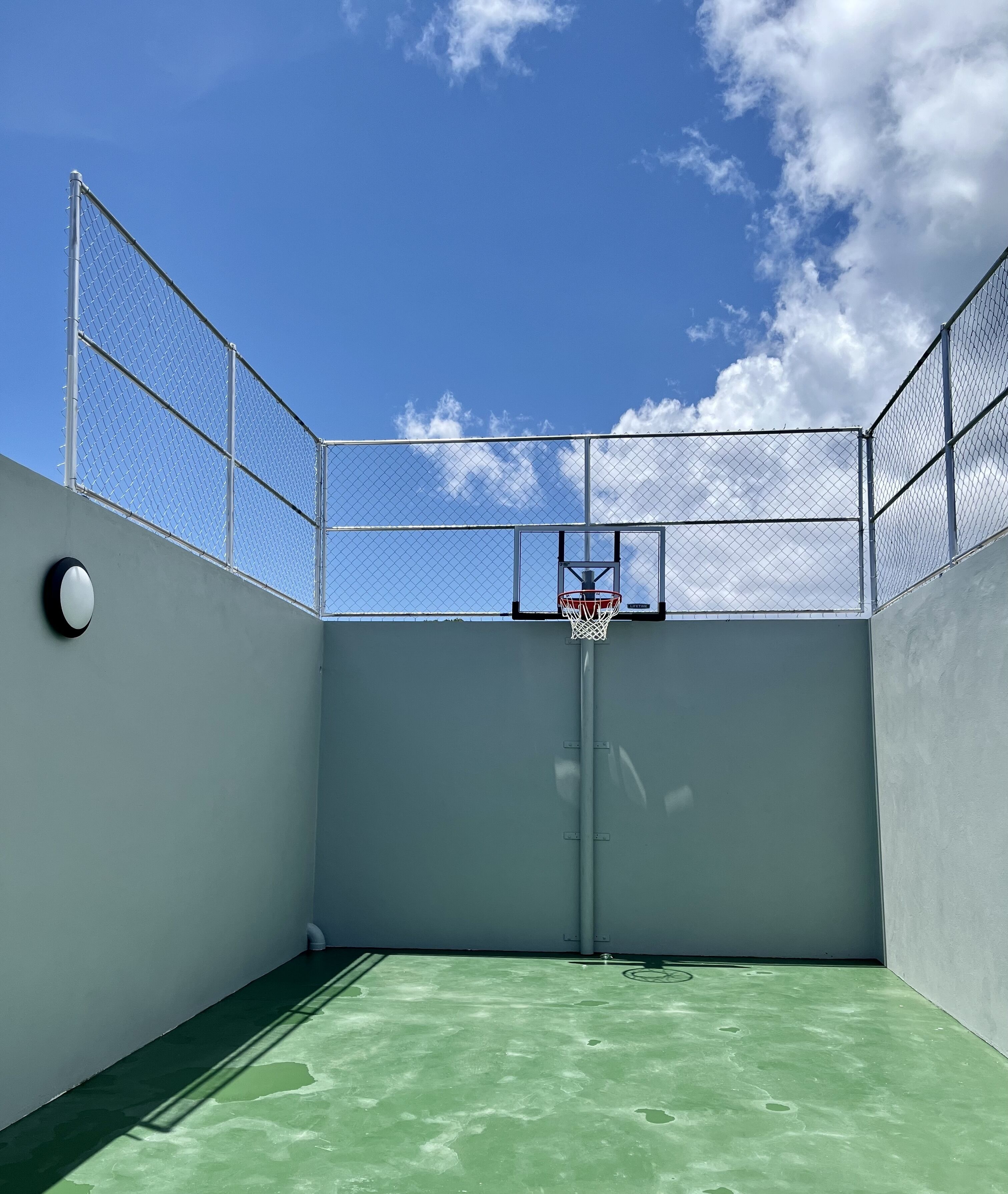 An indoor basketball court with a chain-link fence, a basketball hoop, and a green floor.