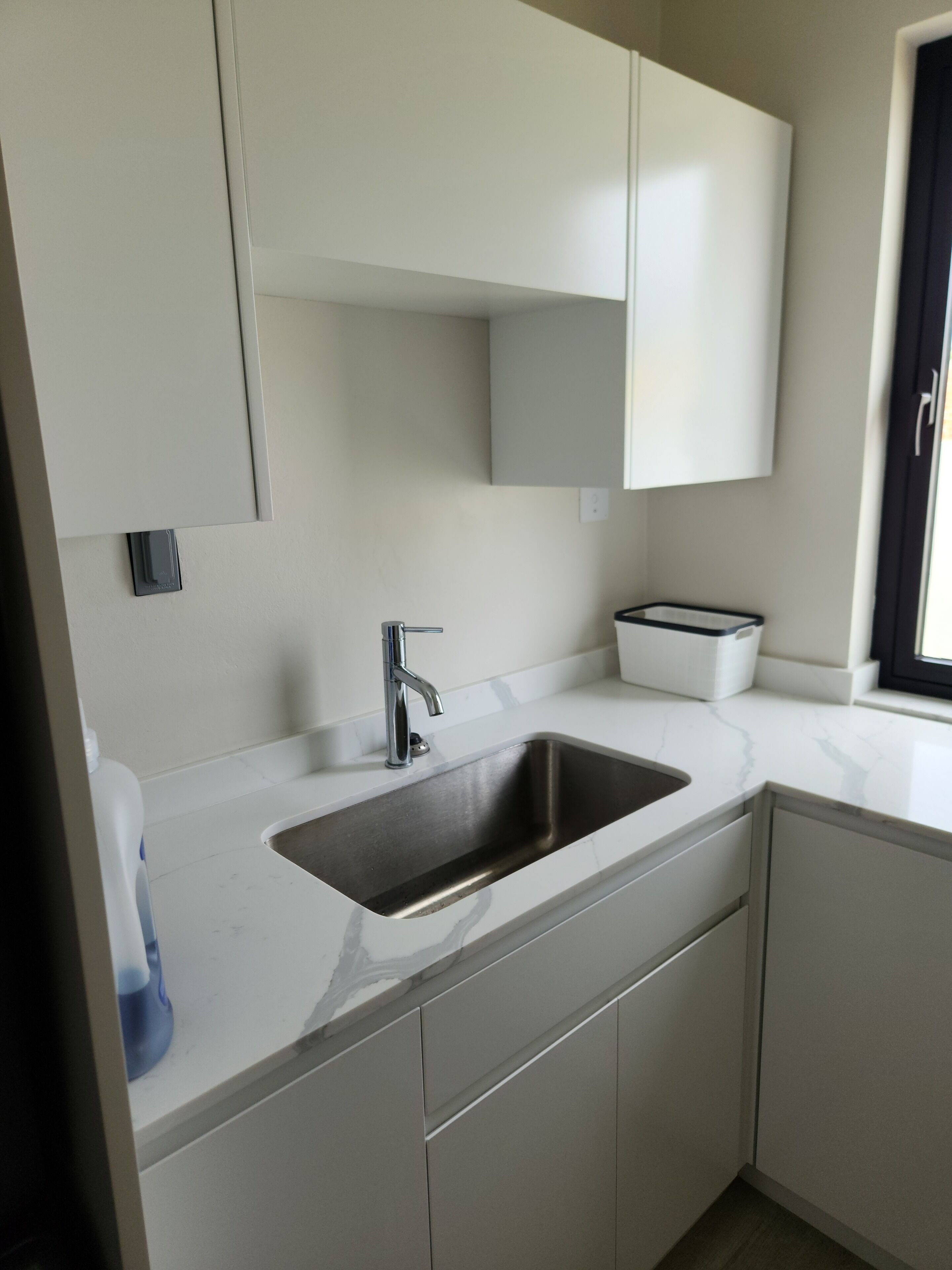 A kitchen with a stainless steel sink, white cabinets, and a window with a view.