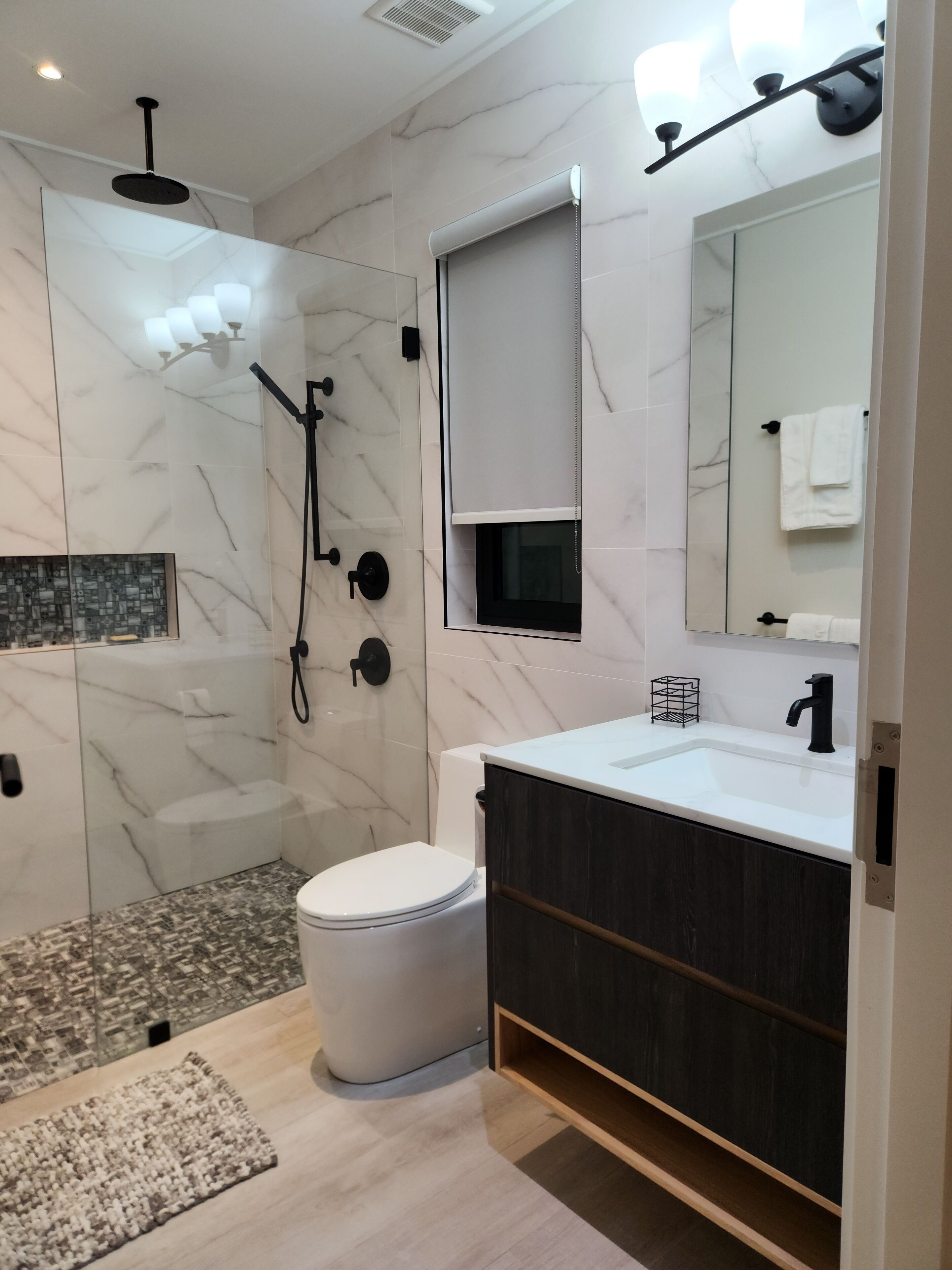 Ein modernes Badezimmer mit einer Glasdusche, Toilette, Waschbecken und einem großen Spiegel.