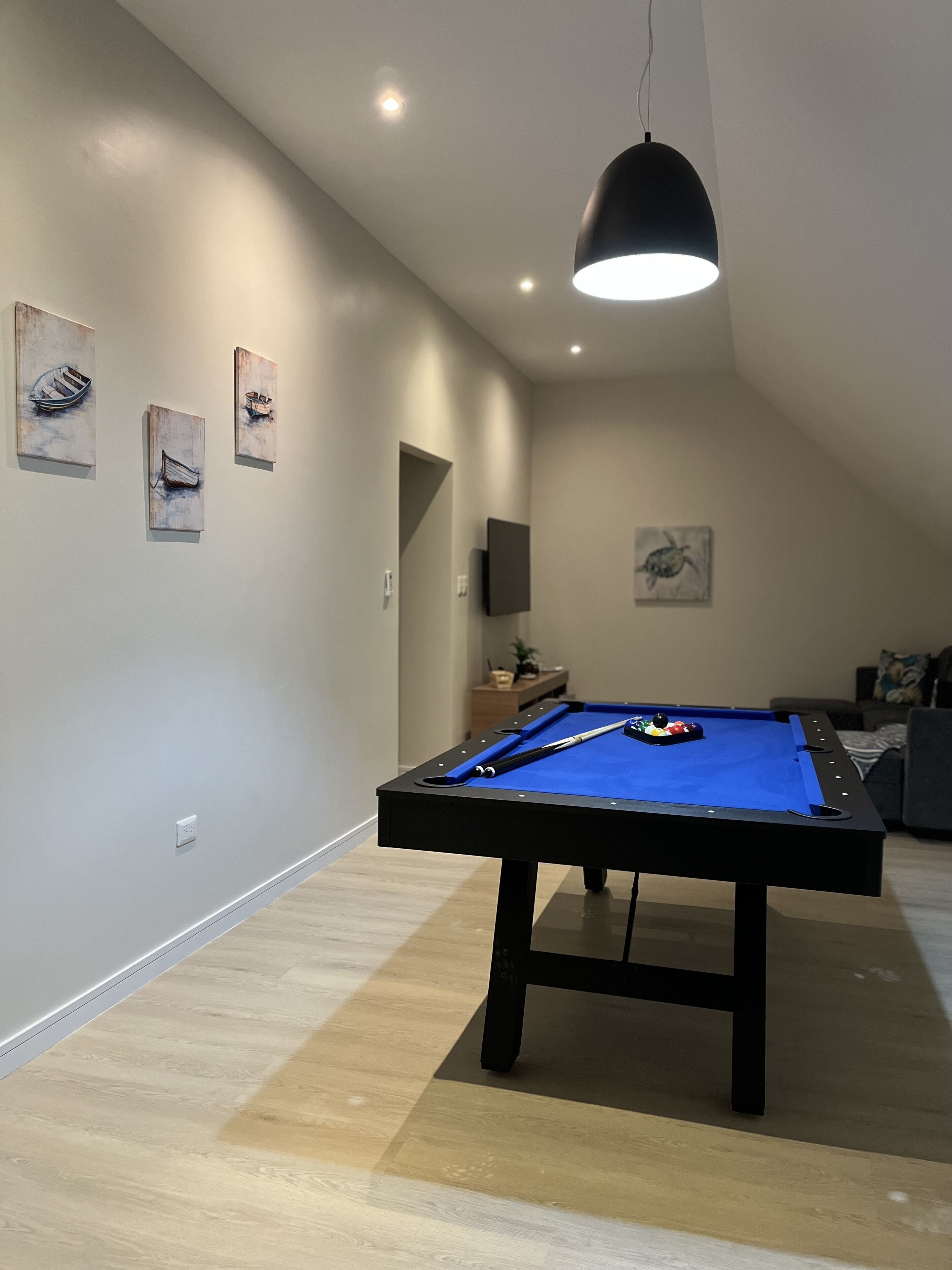 Une table de billard dans une pièce dotée d’un plafond en pente, d’un éclairage encastré et d’œuvres d’art accrochées aux murs.