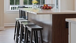 A modern kitchen with a central island, bar stools, a chandelier, and large windows with a view of trees. - NEW Luxury Cottage with Mountain Views (Stanley)