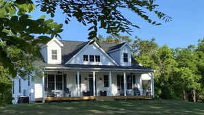 A two-story house with a porch, large windows, and a well-maintained lawn. - NEW Luxury Cottage with Mountain Views (Stanley)