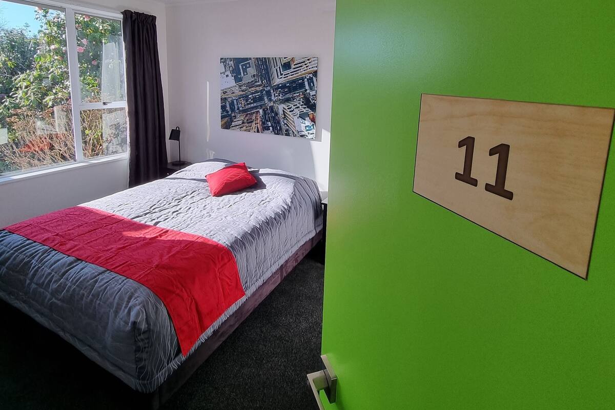 A room with a bed, a window, a green wall, and a number sign.