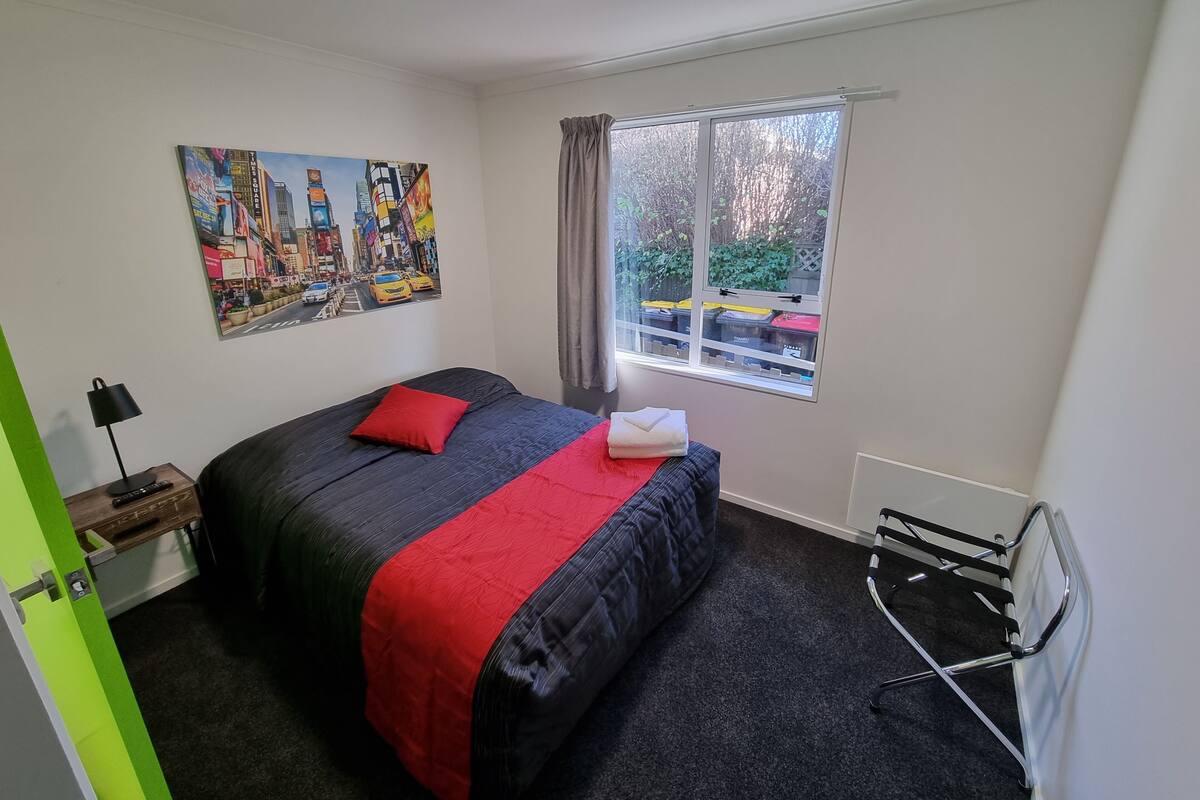 A bedroom with a bed, a window with curtains, a radiator, and a painting on the wall.