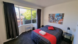 A bedroom with a large bed, a window with curtains, a radiator, and a cityscape painting on the wall. - Stay Timaru (Timaru)