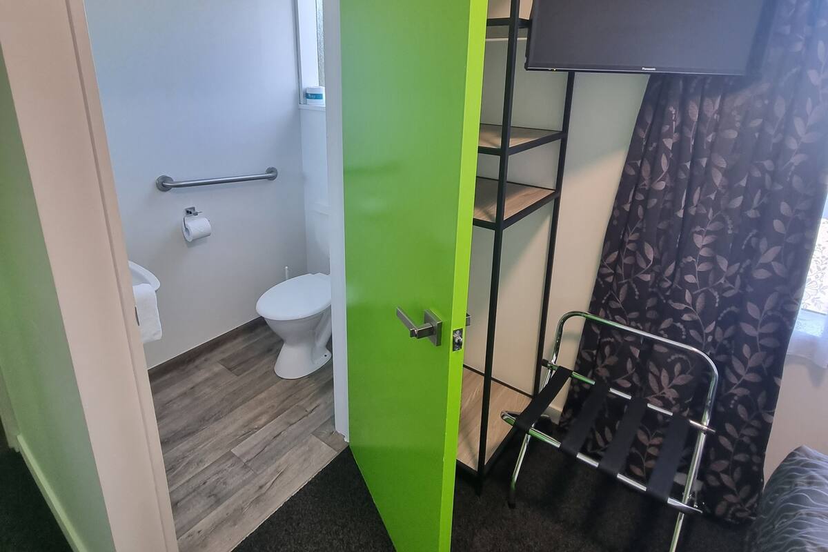 A compact room with a green door leading to a bathroom, a small window, a television on a stand, and a bunk bed with a metal frame.