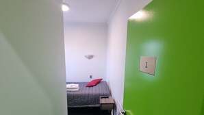 A narrow hallway leading to a room with a bed, a small table, and a green door marked with the number 1. - Stay Timaru (Timaru)