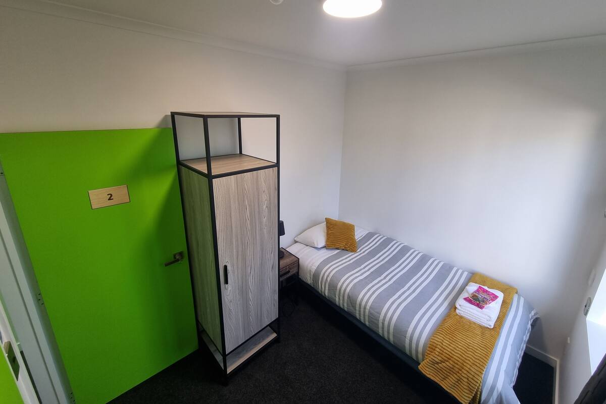A compact room with a bed, a green wardrobe, and a small table.