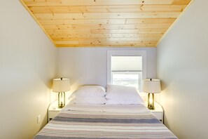 Slaapkamer met schuine plafond, bed met witte lakens, twee bedlampen en een raam met zonwering.