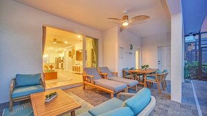 A well-lit outdoor patio with lounge chairs, a table, and a ceiling fan. - Coastal Haven | 7BR, Custom Built Kids Rooms, Arcade, Private Pool (Davenport)